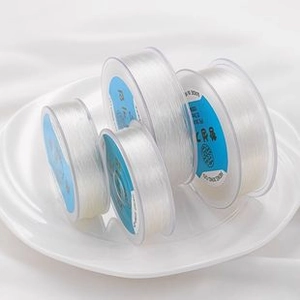 Close-up of four spools of clear elastic beading wire for DIY jewelry on a white plate