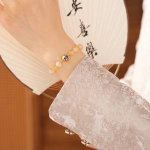 Macro shot of citrine-colored beads bracelet with golden heart-inlaid charm on female wrist