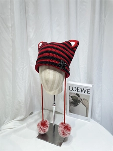 Detail of red and black striped cat ear knit hat with soft hanging pompom tassels