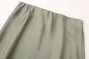 Detail of sage green satin midi skirt showing elastic waistband and silky fabric texture