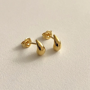 Nahaufnahme minimalistischer goldener Tropfenohrringe mit Hochglanzfinish auf Weiß