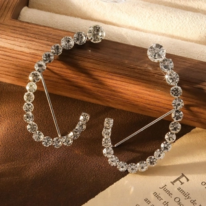 Orecchini a C in argento con strass geometrici pavé su sfondo di libro vintage
