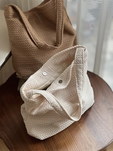 Close-up of herringbone texture and magnetic metal buckle on beige woven canvas bag