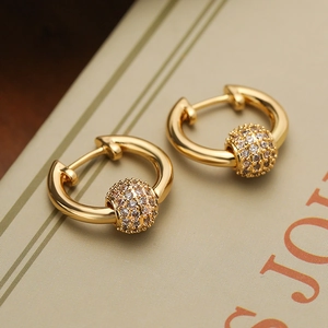 Close-up of gold-plated geometric hoop earrings with a pavé zircon bead on a vintage book