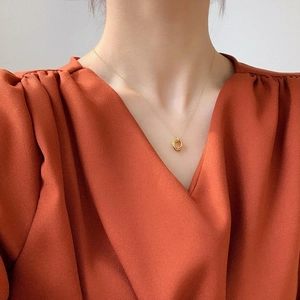 Close-up of minimalist gold double ring necklace on a model wearing an orange V-neck top
