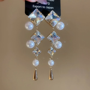Close-up of dangling earrings with square crystals, white pearls and gold teardrop pendants