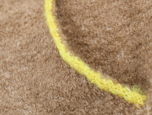 Dettaglio del tessuto in maglia marrone con trama morbida e bordo lavorato giallo brillante