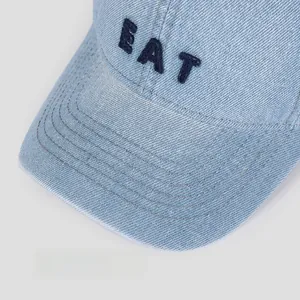 Detail of light blue denim baseball cap with EAT embroidery and stitched brim
