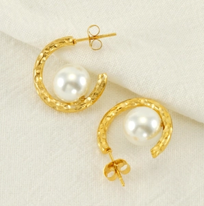 Macro detail of gold hammered C-shaped earrings with large white round pearls