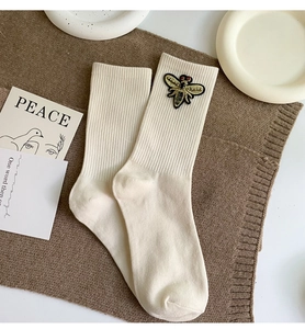 Detail of ribbed knit beige crew socks featuring a delicate 3D bee embroidery patch