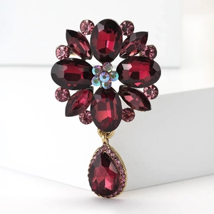 Detail of vintage flower brooch with deep red crystals and teardrop pendant on gold base