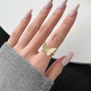 Close-up of golden butterfly ring with white zircons on hand with pink manicure
