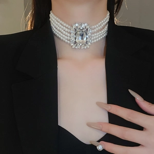 Detail of a multi-layer white pearl necklace with a large crystal centerpiece on a model