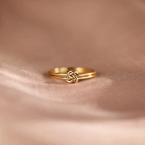 Macro shot of double-layered gold knotted ring on elegant pink silk fabric background