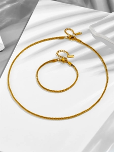 Detail of gold stainless steel necklace and bracelet set with sparkling sand texture