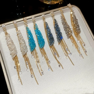 Detail view of crystal tassel earrings in four colors arranged in a beige jewelry box