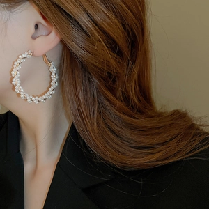 Gros plan de boucles d'oreilles créoles torsadées en perles et fils dorés portées