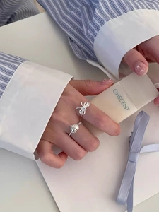 Detail of s925 silver rings with bow and heart designs on a finger, sweet style