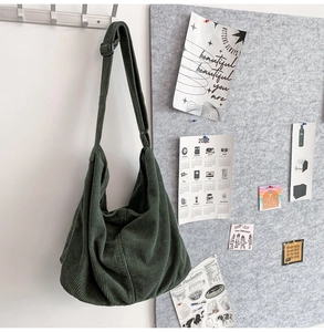 Detail view of a dark green corduroy tote bag hanging on a hook in a minimalist setting