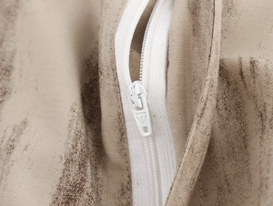 Vista macro di una cerniera bianca su tessuto beige con motivi astratti di colore marrone
