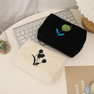 Detail of corduroy floral makeup bags in black and cream colors with embroidery