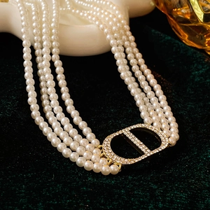 Detail of multi-layer pearl necklace with a gold crystal-encrusted CD letter charm