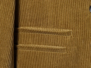 Detailed view of yellow corduroy fabric jacket featuring precision pocket stitching
