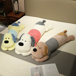 Trois coussins longs en peluche chien rayé en jaune, blanc et marron sur un lit