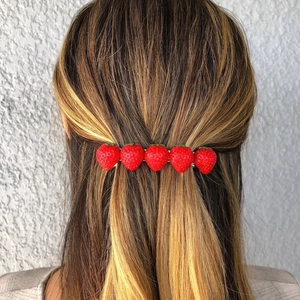 Detailed view of a handmade strawberry hair clip worn on the back of a woman's head