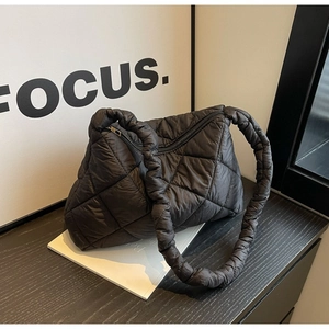 Detailed view of black quilted puffer bag on a wooden desk with a minimalist background