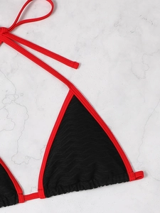 Detail of black wavy textured bikini top with red trim and ties on marble background