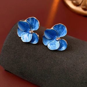 Gros plan sur des boucles d'oreilles fleur en émail bleu avec bords dorés et cristaux