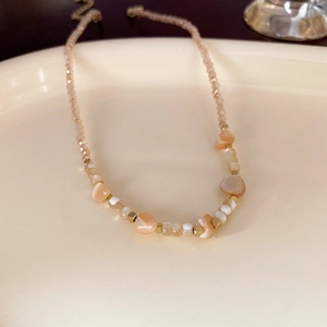 Elegante Perlenkette mit champagnerfarbenen Kristallen und goldenen Perlen auf Keramik