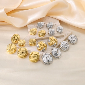Close-up of golden and silver irregular textured earrings on stone and silk background