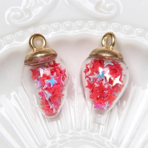 Waterdrop glass pendants with red star sequins and gold metal caps on ceramic tray