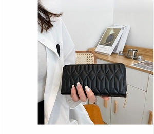 Detail of a black quilted long purse with zipper closure held by a model for size