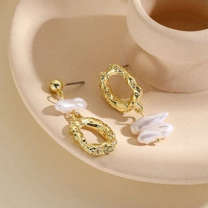 Macro shot of gold textured lava rings and baroque pearls on beige ceramic dish
