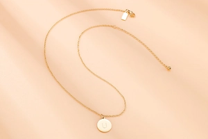 Détail d'un collier en acier doré avec un pendentif rond orné de la lettre U gravée