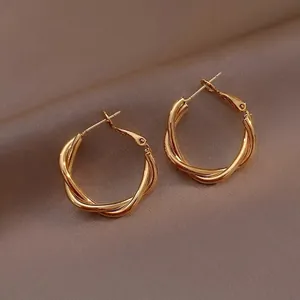 Detail of twisted gold hoop earrings showing textured braided design on brown fabric