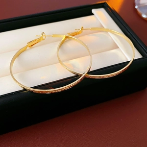 Macro shot of gold-plated large hoop earrings with frosted texture in luxury black gift box