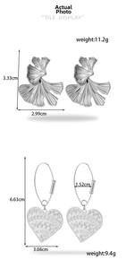 Close-up of silver ginkgo leaf studs and hollow vintage heart drop earrings on white background