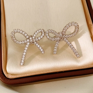Macro shot of sparkling zircon bow clip earrings on elegant silk jewelry box lining