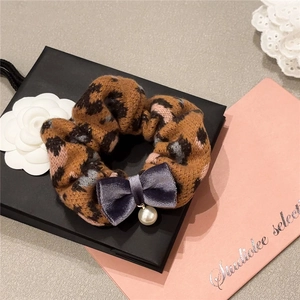 Leopard print scrunchie with a dark purple velvet bow and pearl pendant on a gift box
