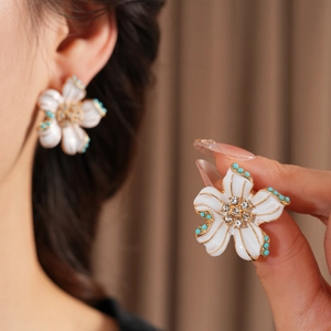 Gros plan sur des boucles d'oreilles vintage en émail blanc avec détails dorés et turquoise