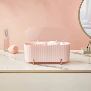 Pink vertical stripe cotton pad organizer with gold legs and clear lid on marble