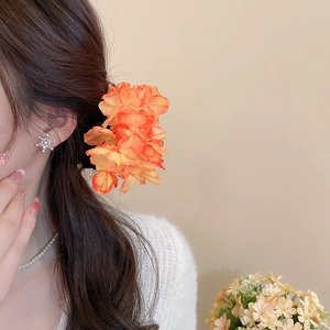 Close-up of elegant orange fabric flower hairpin and snowflake stud earring on model