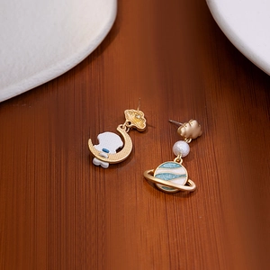 Detail of asymmetric astronaut earrings with moon and planet pendants on wood