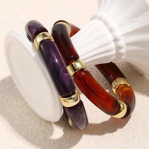 Retro acrylic stretch bracelets with marble texture and golden beads on white pedestal