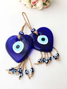Detail of two heart-shaped blue glass evil eye charms with jute rope tassels on white surface