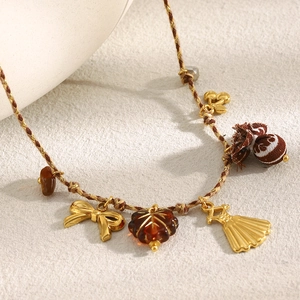 Détail d'un bracelet tressé marron avec pendentifs dorés et feuilles en résine ambre